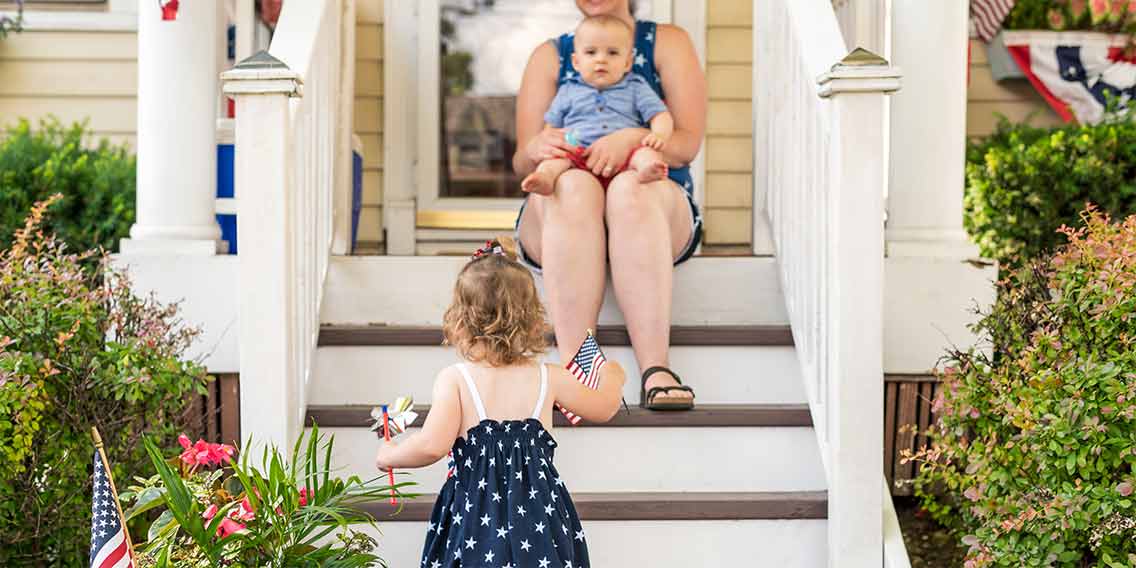Child with American flag running up steps of home.