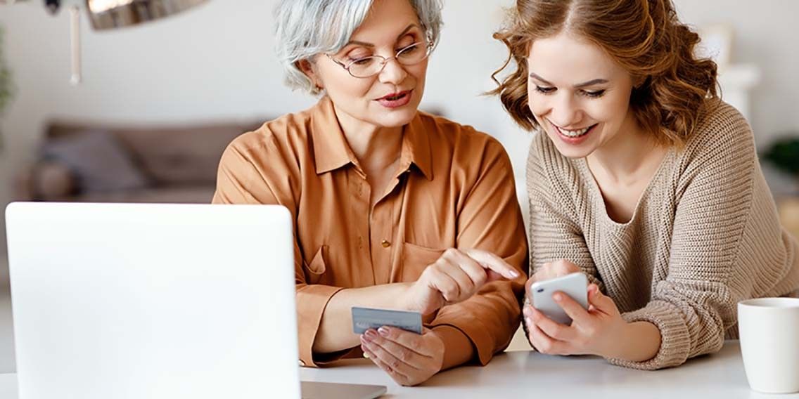 younger woman helping older woman with mobile banking