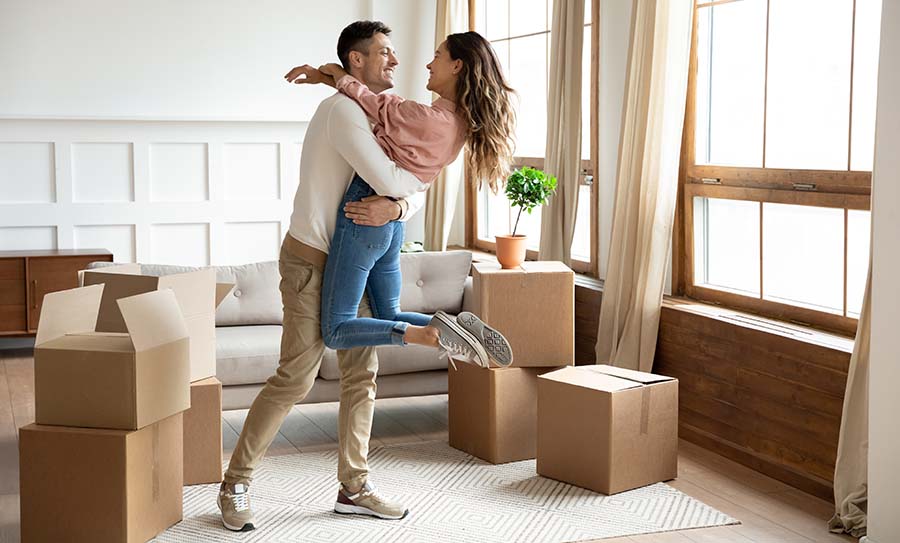 Happy husband lifting excited wife celebrating moving day with boxes