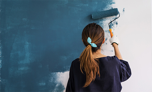 Woman painting wall with a paint roller.