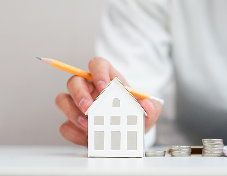 hand on model of home with pencil in hand
