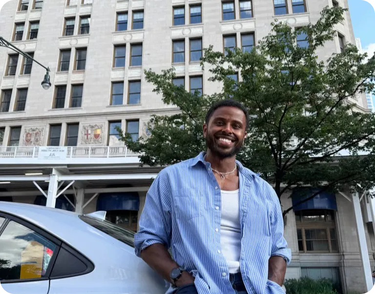 Person standing outside, leaning against back of the car and smiling.