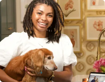  Lady standing with a dog and smiling, with a background of a wall filled with hung picture frames