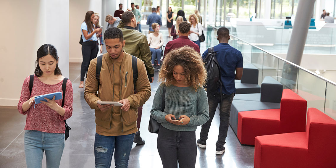 Students walk in university campus using tablets and phone