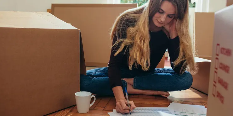 Woman writing and sitting with moving boxes.