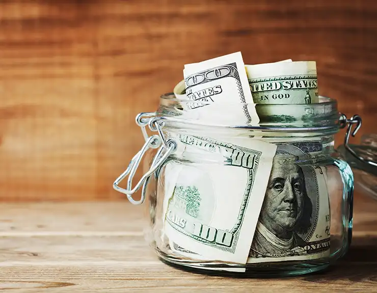 Dollar bills in glass jar on wooden background. Saving money concept.