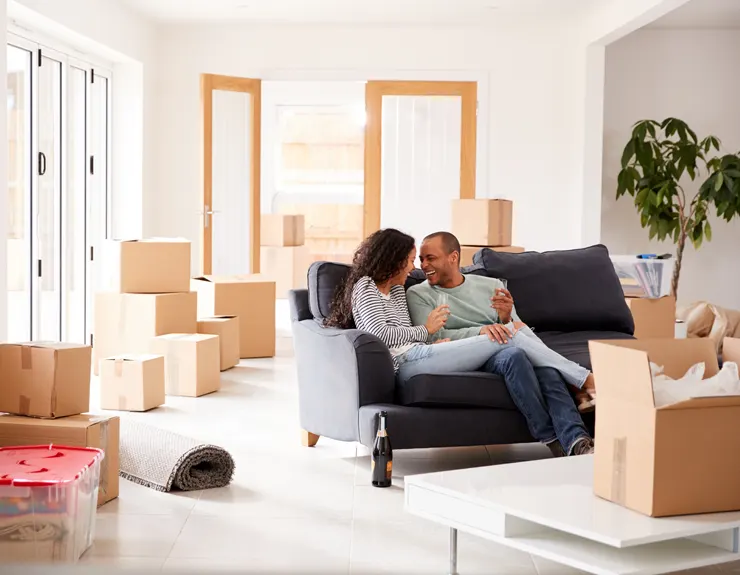 Young men and women sitting on sofa in a new house, with moving boxes around