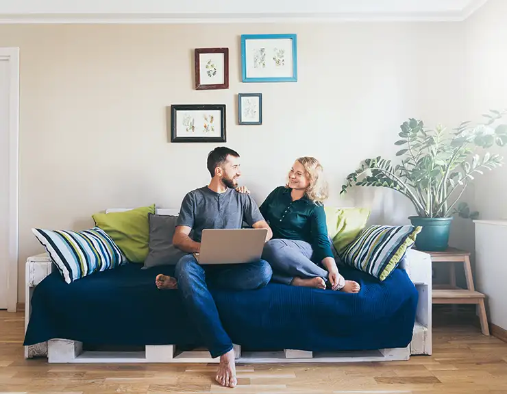 Young couple doing shoppings online on the sofa at home with laptop, looking at each other and smiling