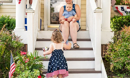 child with American flag running up steps of home