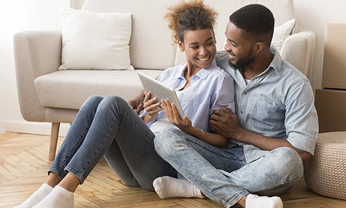 Man and woman seated on floor looking at their tablet computer.