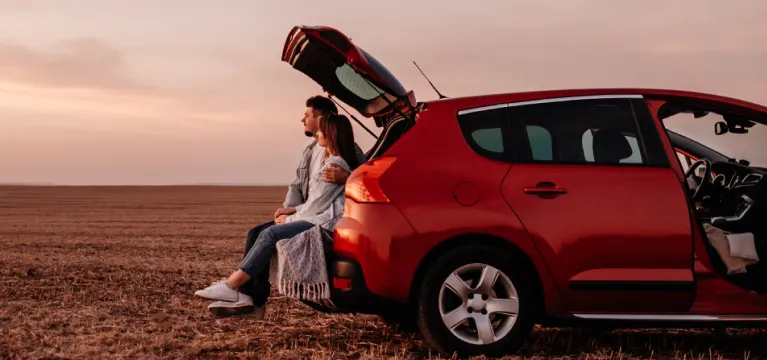 Happy couple sitting in trunk of their new car in countryside