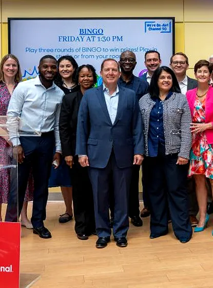 A diverse group of professional executives posing together in front of a digital presentation board for PenFed Credit Union.