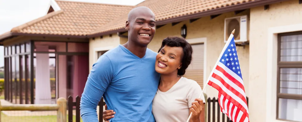 Couple standing in front of their home with the American flag on their flagpole