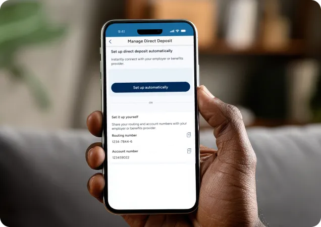 A person's hand holding a smartphone displaying the PenFed mobile app screen for managing and setting up a direct deposit.