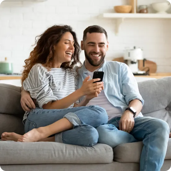 Happy couple seating on sofa and looking at the phone screen