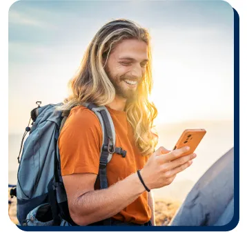 Smiling hiker with backpack looks at smartphone outdoors, illustrating PenFed personal loans for travel and adventure.