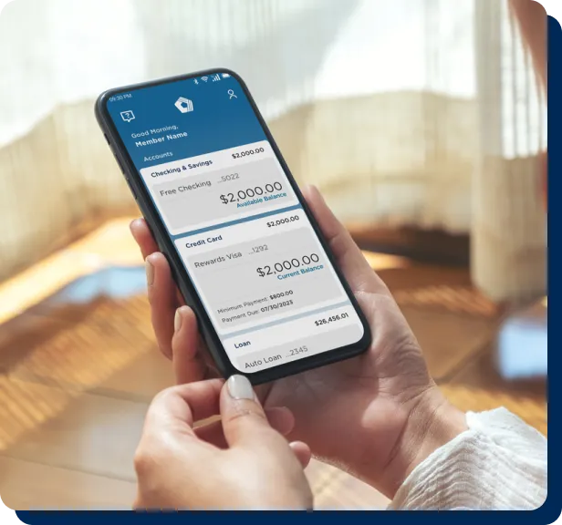 A person holds a smartphone displaying the PenFed mobile app dashboard with checking, credit card, and auto loan account balances.
