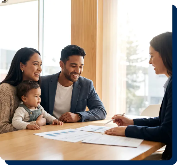 A smiling young family with a baby meets with a PenFed loan officer at a desk to review financial documents.