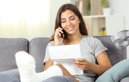 woman in cast looking at paper while on the phone