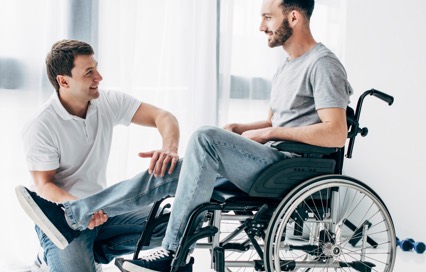 man in wheelchair smiling at therapist who’s raising his leg