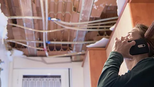 man on phone looking at a hole in the roof