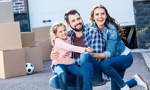 Family of three posing in the driveway while moving in home