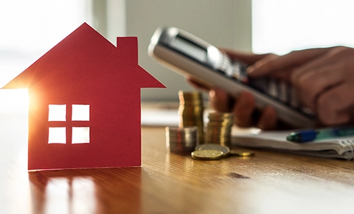 model paper home on desk next to coins and a calculator