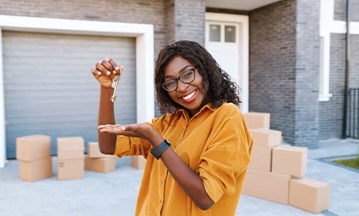 Woman holding new home keys, while moving boxes kept in front of the garage