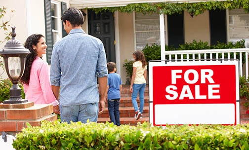 family in front of home with for sale sign