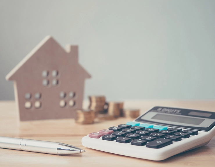 Calculator with wooden house and coins stack and pen on wood table. Property investment and house mortgage financial concept