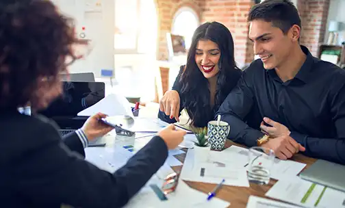 Young beautiful couple applying for mortgage. Sitting smiling happy meeting with real state agent considering mortgage loan at