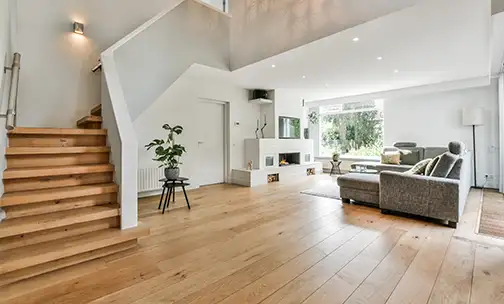 Cozy house interior with a wooden floor, large gray sofa, and stairs leading to the second floor